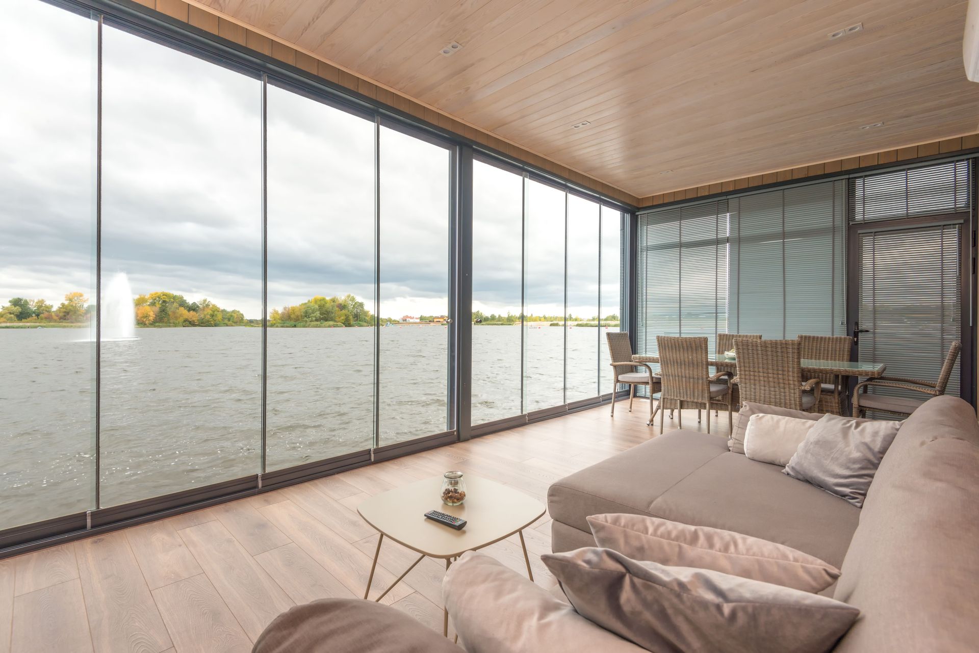 Interior of spacious modern villa with comfortable sofa and glass walls overlooking wavy lake under cloudy sky