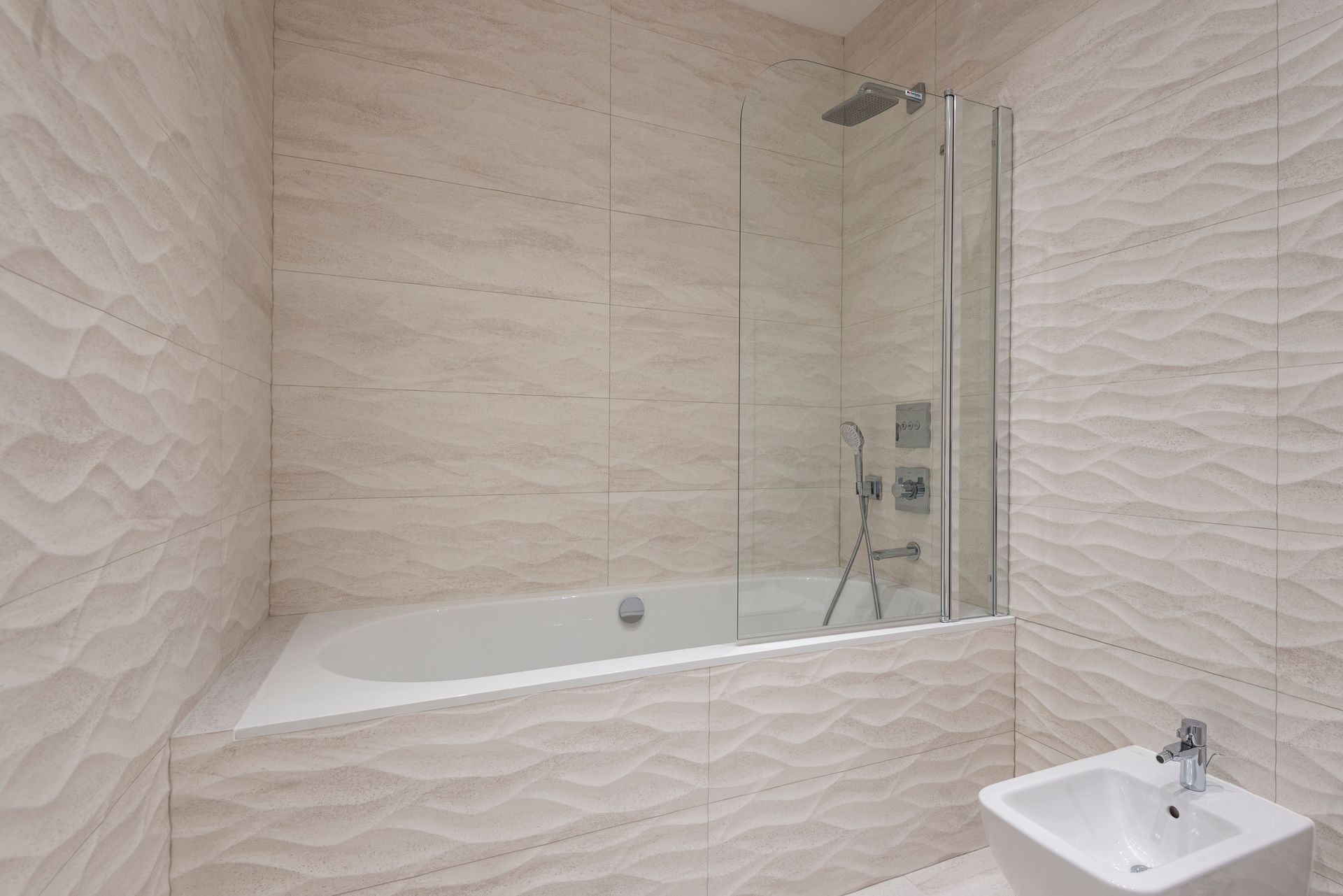A sleek modern bathroom featuring a bathtub, shower, and beige textured tiles.